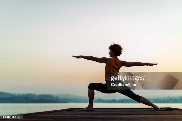 frau beim yoga in der nähe des sees bei sonnenuntergang - woman stretching sunset stock-fotos und bilder