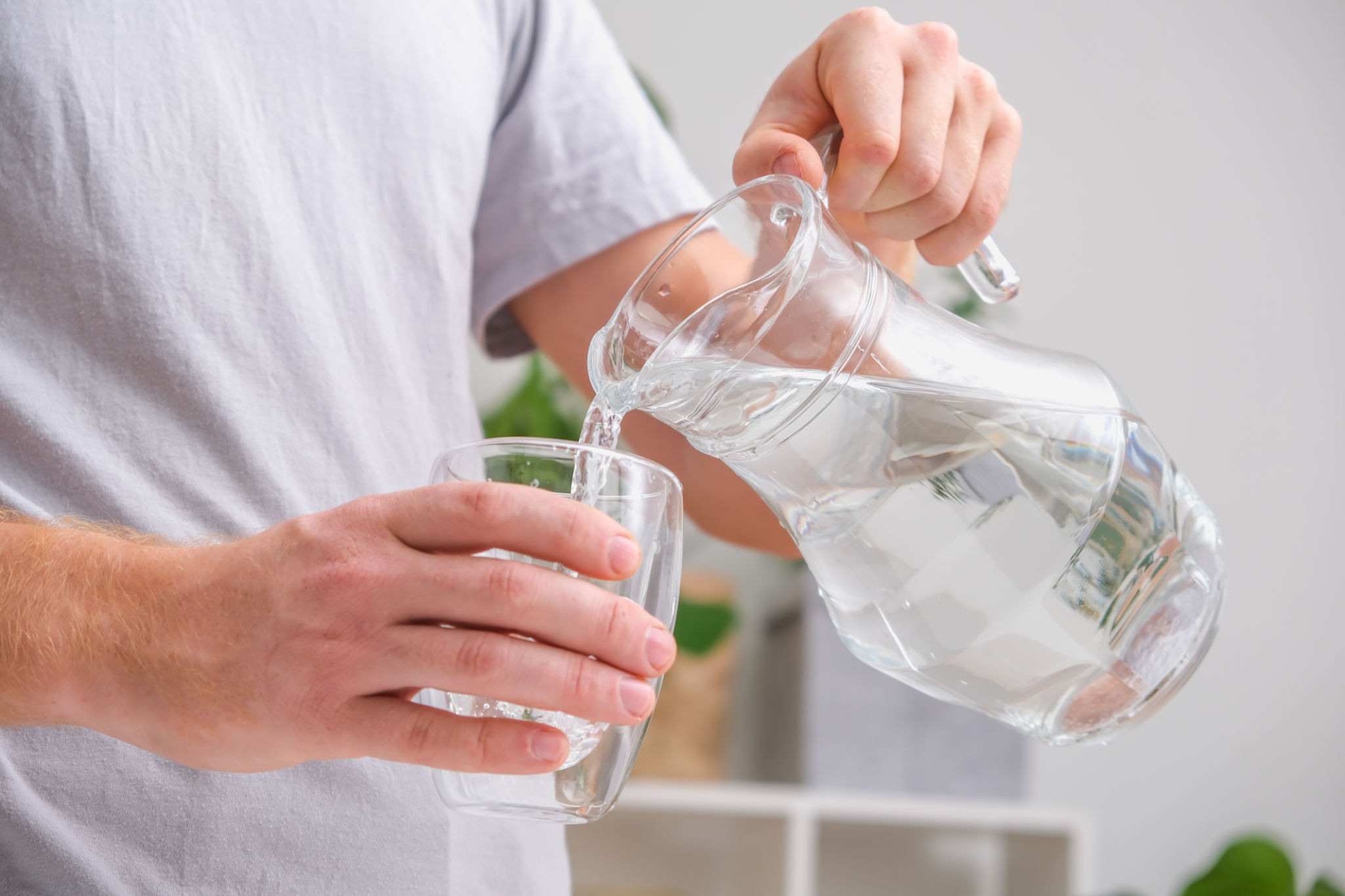 Man pours cold water into glass. Close-up of male hands pouring water from a jug into glass tumbler. Man pours cold water into glass. Close-up of male hands pouring water from a jug into glass tumbler.