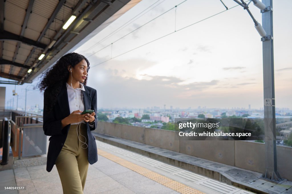 Hombre de negocios de pie y esperando el tren mientras escucha música en auriculares.