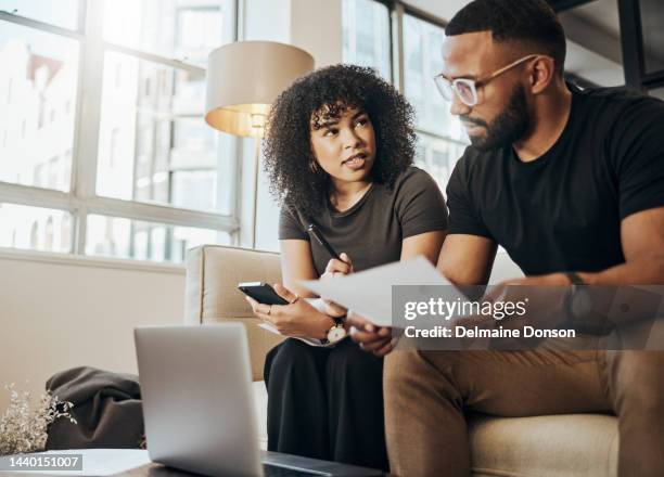 finance, tax and couple talking about insurance, savings and information on a laptop with paper. man and woman on the sofa of their house for ecommerce, banking and investing with technology - forced marriage stockfoto's en -beelden