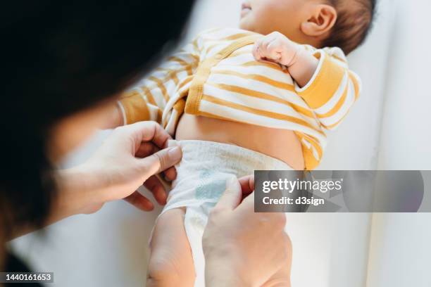 over the shoulder view of young asian mother taking care and changing the diaper for her baby at home. new life. love, care and tenderness - changing diaper stock-fotos und bilder