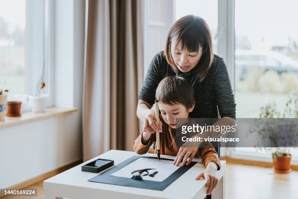 japanese mother and son writing traditional calligraphy - japanese calligraphy stock pictures, royalty-free photos & images