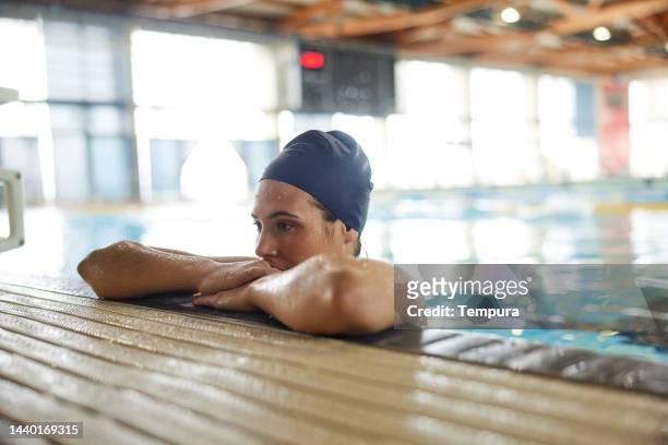 seitenansicht porträt müde und desillusioniert 
junge schwimmerin hängt nach niederlage im schwimmwettbewerb über dem pool - female swimmer stock-fotos und bilder