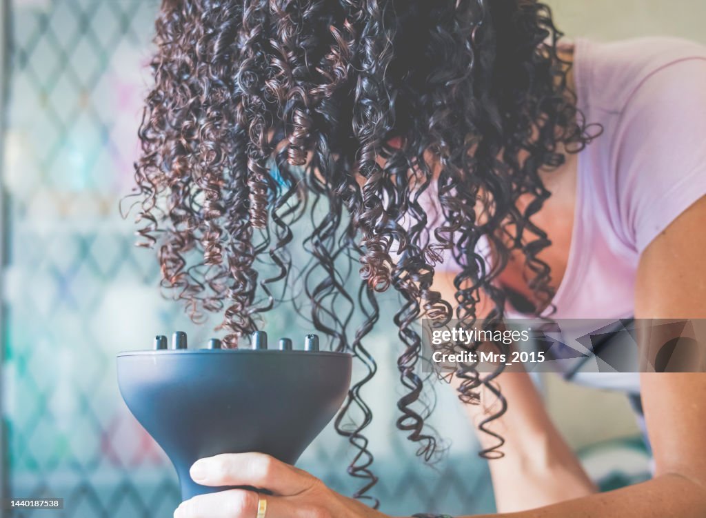 Close-Up of a woman bending over and drying her curly hair with a hair diffuser