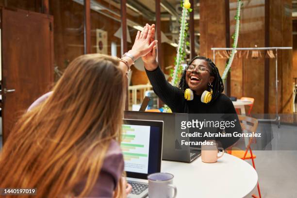 two work colleagues giving each other high-five to express success while sitting at their workstations - efficiency photos et images de collection
