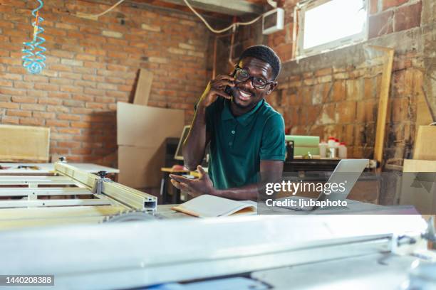 young carpenter answering smart phone at work. - small office building stock pictures, royalty-free photos & images