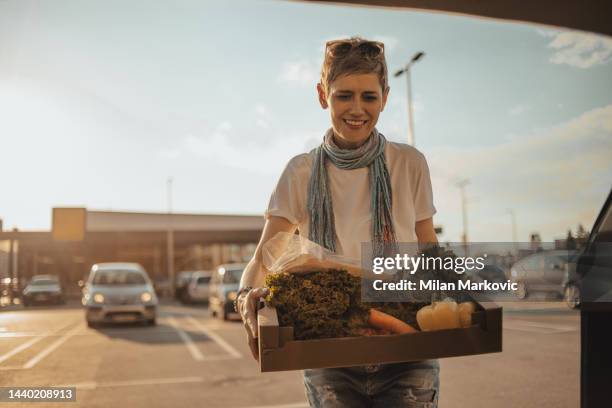 a mature woman is leaving a box of vegetables in her car in the parking lot in front of a supermarket, she has just finished shopping. - groenteboer stockfoto's en -beelden