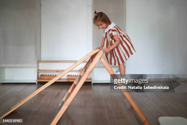 child girl in striped dress in kindergarten rides down slide and climbs stairs. physical development of children. walking up the stairs. - spielplatz einrichtung stock-fotos und bilder