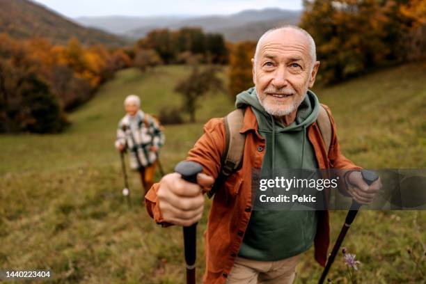 senior man on a hike with his wife behind him - hiking pole stockfoto's en -beelden