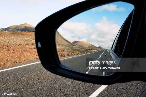 road leading into the distance reflected in rear view mirror in volcanic landscape - rear view mirror stock pictures, royalty-free photos & images