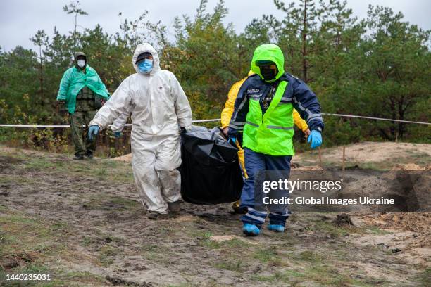 Forensic technicians with policemen carry a black body bag at the site of a mass burial on October 11, 2022 in Lyman, Ukraine. The exhumation was...