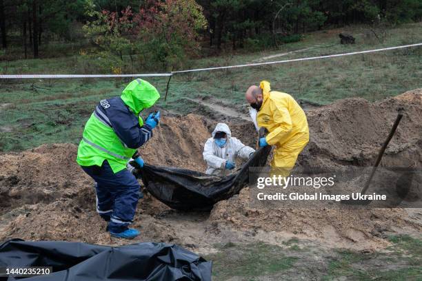 Forensic technician with policemen raise a black body bag from exhumed grave at the site of a mass burial on October 11, 2022 in Lyman, Ukraine. The...