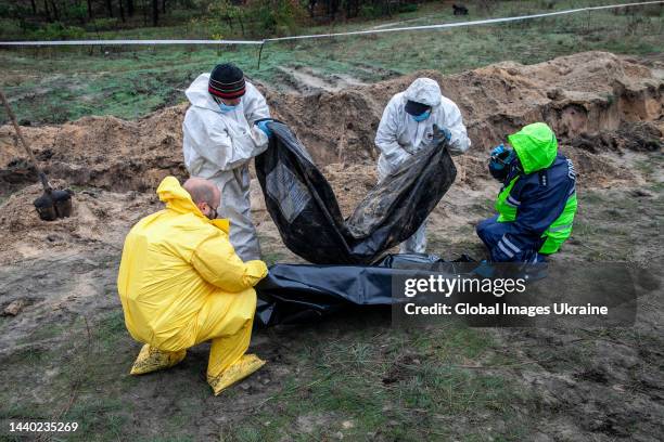 Forensic technicians with policemen hold a black body bag with exhumed body at the site of a mass burial on October 11, 2022 in Lyman, Ukraine. The...