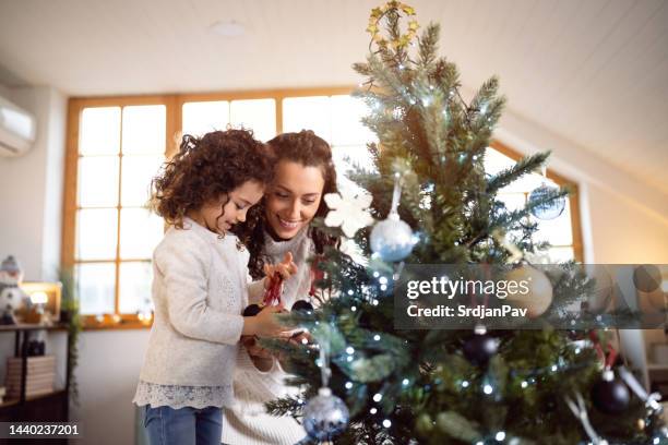 figlia e madre caucasiche che decorano l'albero di natale - decorare l'albero di natale foto e immagini stock