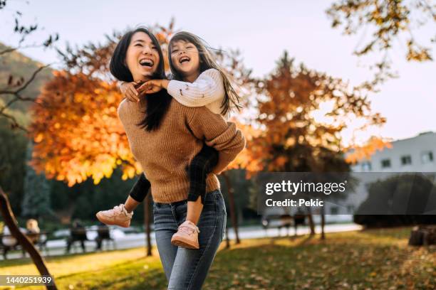 aufnahme eines entzückenden kleinen mädchens, das mit ihrer mutter eine huckepackfahrt im öffentlichen park genießt - happy family asian stock-fotos und bilder