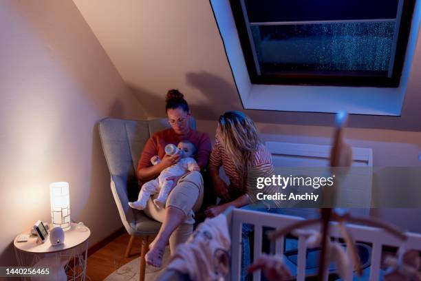 lesbian couple putting baby to sleep in the nursery - nursery night stock pictures, royalty-free photos & images