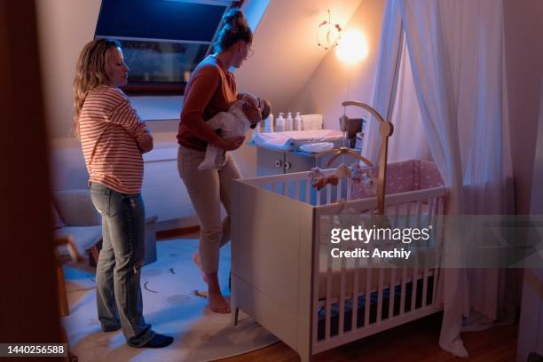 female gay couple putting baby to sleep in the nursery - nursery night stock pictures, royalty-free photos & images