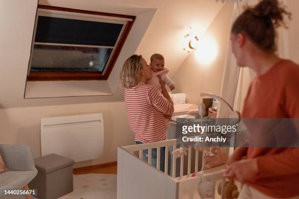 two beautiful moms kissing their baby girl before bedtime - nursery night stock pictures, royalty-free photos & images