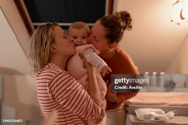two beautiful moms kissing their baby girl before bedtime - lullaby stock pictures, royalty-free photos & images