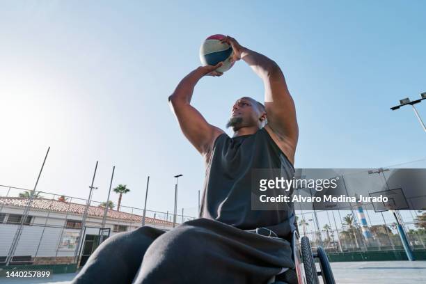african american male wheelchair basketball player shooting basket on an outdoor court. - shooting baskets stock pictures, royalty-free photos & images