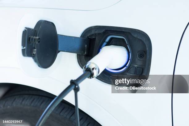 cable plugged into an electric car, charging the batteries on the street. electric car charging, renewable energy, sustainability and transportation concept. - fahrzeug mit hybrid antrieb stock-fotos und bilder