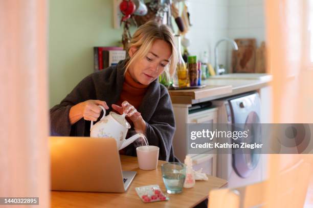 woman with cold symptoms working from home, pouring herself some hot tea - cough lozenge stock pictures, royalty-free photos & images