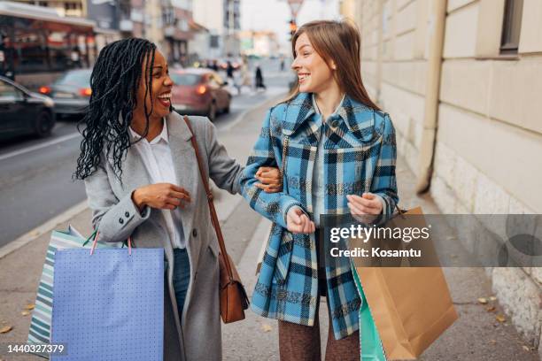 two happy women have crazy fun walking through town after a successful shopping spree - winter coat stock pictures, royalty-free photos & images