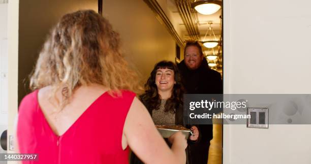 woman welcoming guests to friendsgiving potluck - thanksgiving arrival stock pictures, royalty-free photos & images