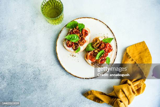 overhead view of a glass of fig lemonade and two slices of bread with feta cheese, roasted tomatoes and basil - food styling foto e immagini stock