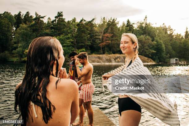 smiling woman wearing towel while looking at female friend during vacation - jetty lake stock pictures, royalty-free photos & images