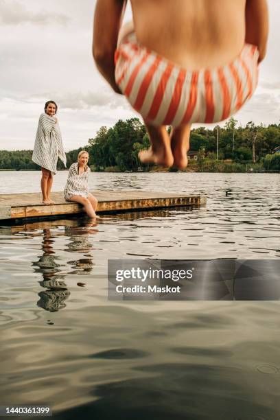 women at jetty looking at male friend jumping in lake during vacation - stockholm summer stock-fotos und bilder