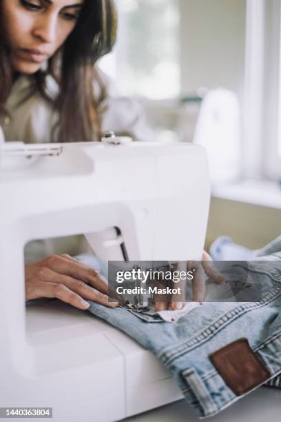 female fashion designer sewing fabric on jeans pocket using sewing machine at workshop - pantalon stockfoto's en -beelden