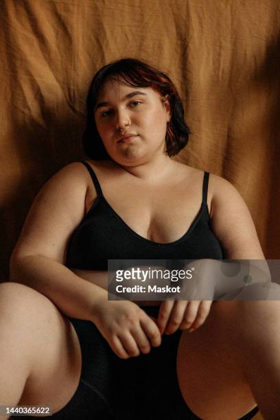 portrait of confident voluptuous woman wearing black lingerie while sitting at home - heavy set women stock pictures, royalty-free photos & images