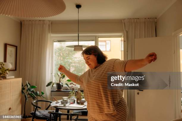 smiling carefree young woman with arms outstretched dancing at home - fat woman dancing stockfoto's en -beelden