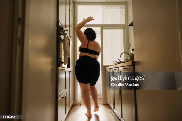 rear view of young voluptuous woman with hand raised dancing in kitchen - bra stock pictures, royalty-free photos & images