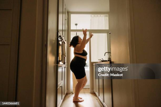 young voluptuous woman with arms raised enjoying dance in kitchen - body positive stockfoto's en -beelden