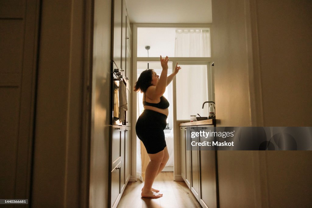 Young voluptuous woman with arms raised enjoying dance in kitchen