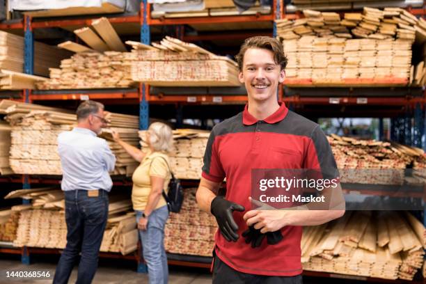 portrait of smiling salesman holding glove while standing in front of rack at hardware store - bouwmateriaal stockfoto's en -beelden