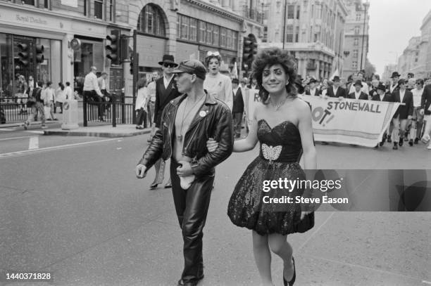 Two marchers in contrasting leather and bubble skirt outfits, ahead of a banner promoting the LGBT rights charity, Stonewall, at the Lesbian and Gay...