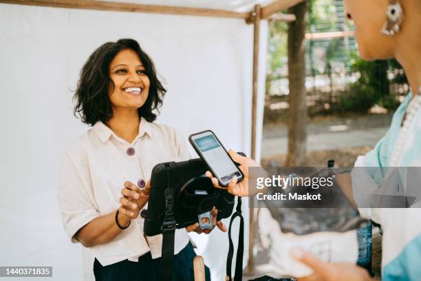 happy female owner communicating with customer doing mobile payment at flea market - apple pay mobile payment stock-fotos und bilder