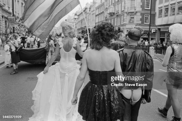Marchers in a variety of outfits, one carrying a rainbow flag , during the Lesbian and Gay Pride event, London, 18th June 1994.