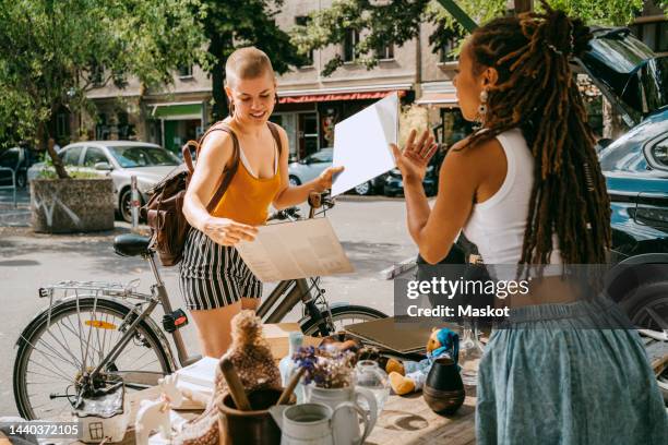 female owner communicating with customer holding records while shopping at flea market - elektromarkt stockfoto's en -beelden