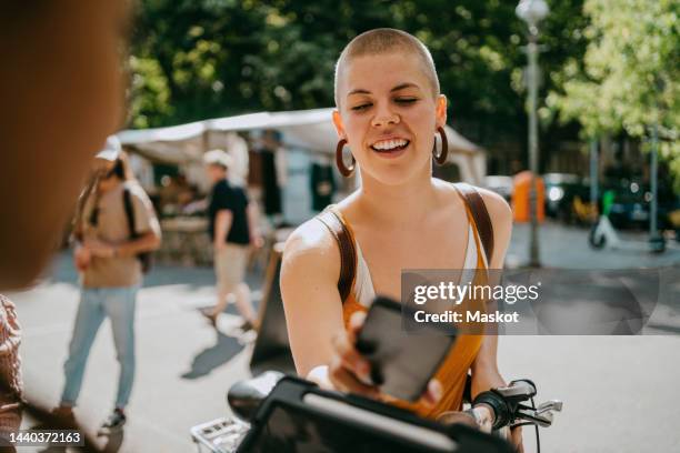 smiling woman with shaved head paying via tap to pay while shopping at flea market - apple pay stock pictures, royalty-free photos & images