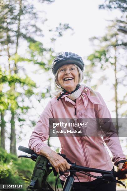 smiling senior woman looking away while standing with cycle - alleen seniore vrouwen stockfoto's en -beelden