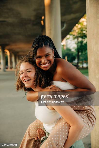 portrait of happy teenage girl giving piggyback ride to female friend - alleen tieners stockfoto's en -beelden