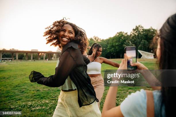 teenage girl photographing happy female friends dancing in park - alleen tieners stockfoto's en -beelden
