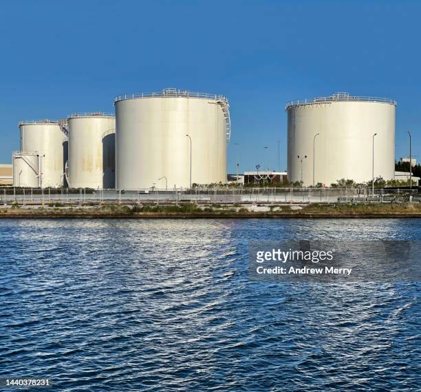 white fuel storage tanks, river reflections blue sky - punishment stocks stock pictures, royalty-free photos & images