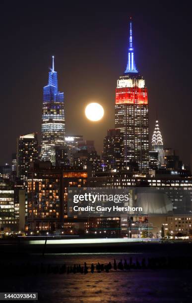 Percent illuminated Beaver Moon rises behind the Empire State Building, lit in red, white and blue in honor of the USA men's World Cup soccer team,...