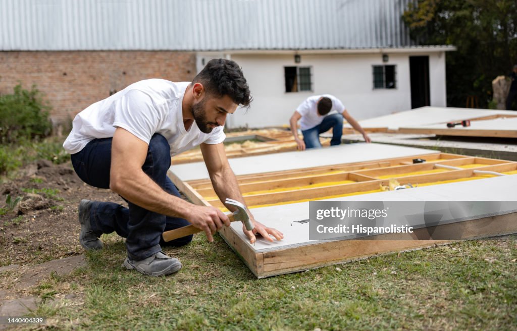 Man volunteering to build a house and hammering a nail on a wooden panel