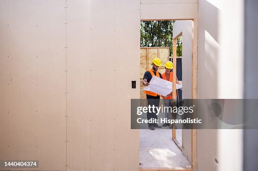 Construction workers looking at blueprints while building a house Construction workers looking at blueprints while building a house